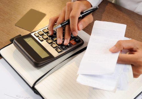 Closeup of person holding bills and calculating them Closeup of person holding bills and calculating them. Notebook, calculator and credit card lying on desk. Payment concept. Cropped view.