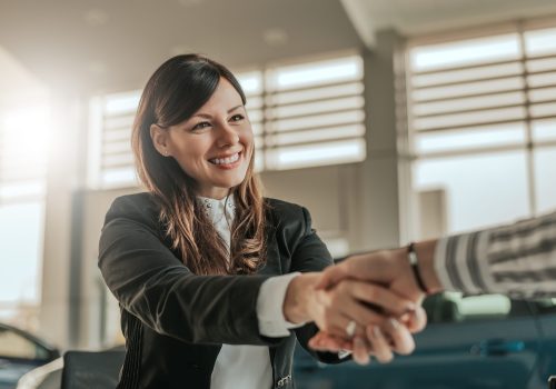 Cheerful car dealer handshake with customer in showroom.
