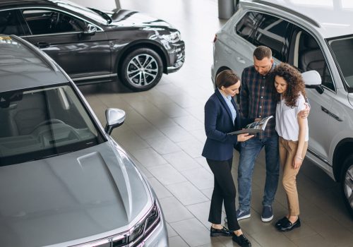 Young couple talking to a sales person in a car showroom